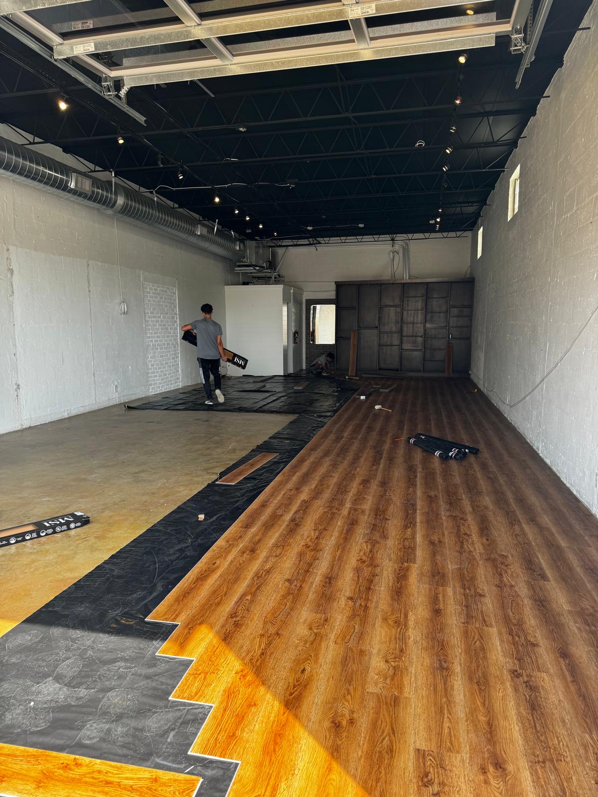 Large open warehouse floor mid-install with dark oak luxury vinyl plank