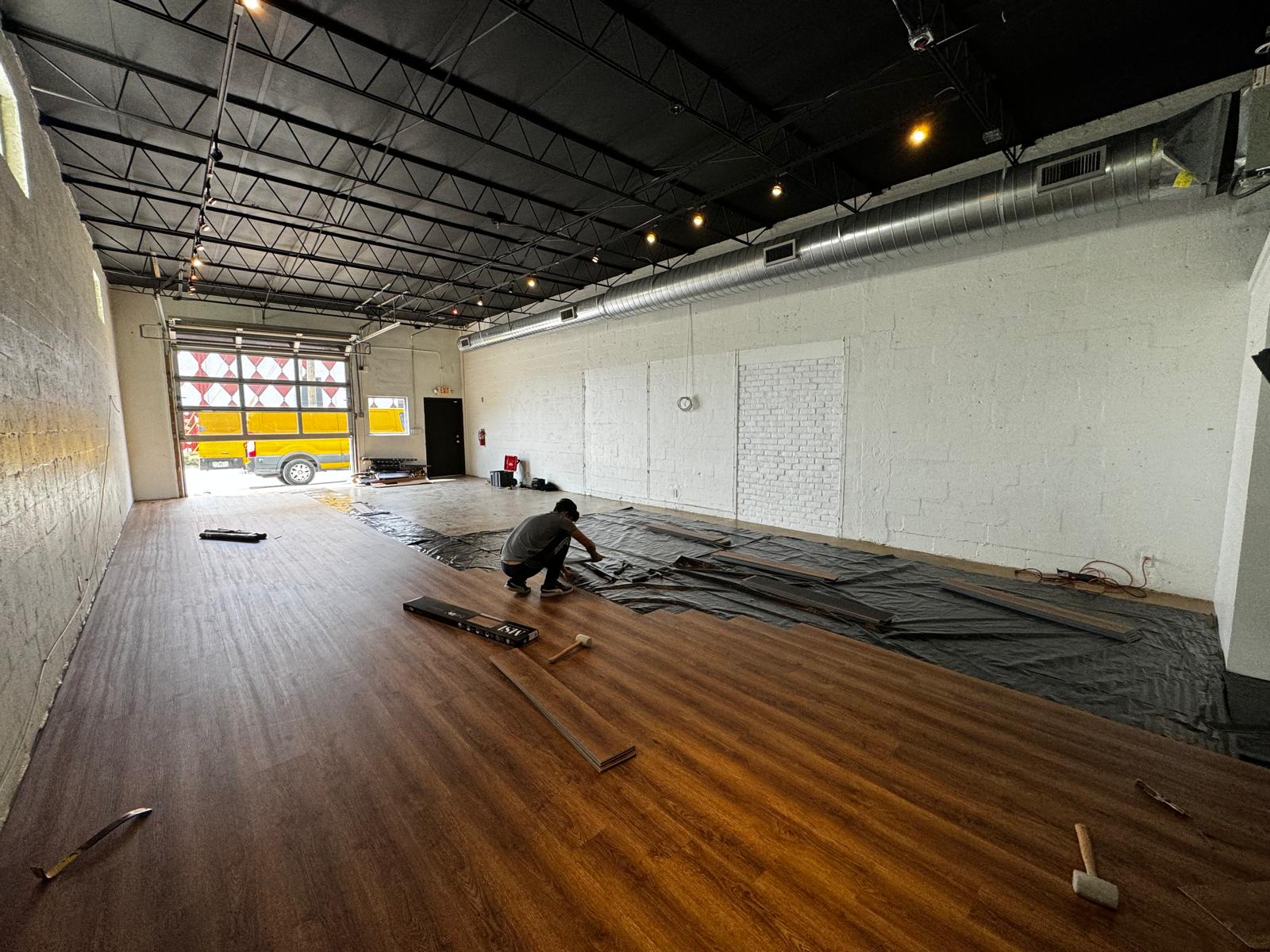 Wide commercial bay with dark walnut LVP being laid toward the loading door
