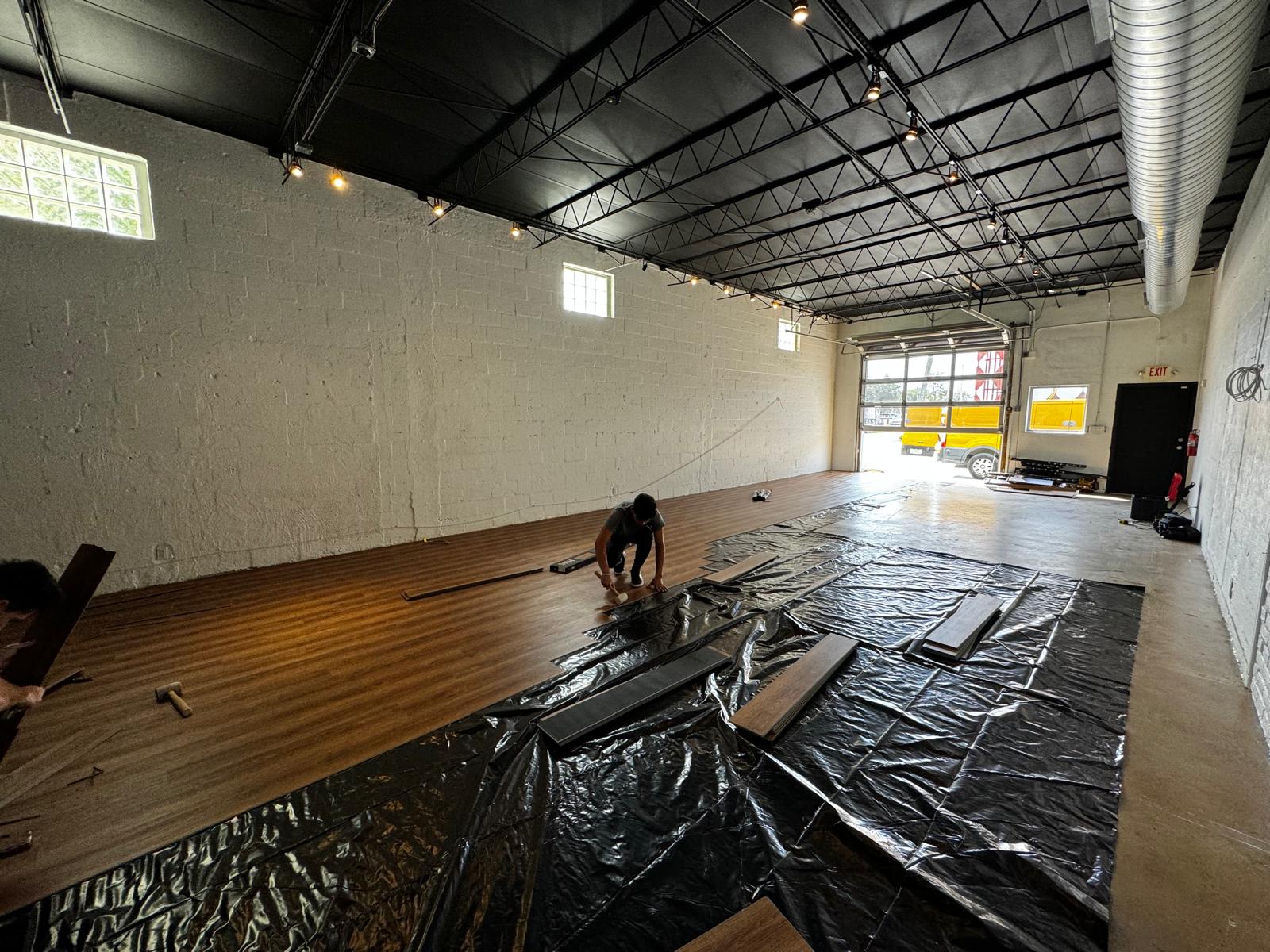 Installer fitting the next row of warm walnut LVP across a large open floor